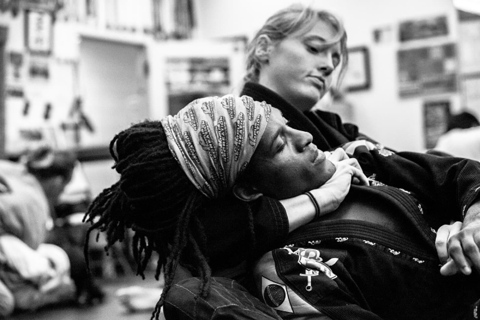 Two women training jiu-jitsu, one controlling from behind